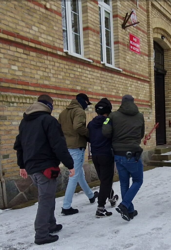 Policjanci doprowadzają podejrzanego do Sądu Rejonowego w Giżycku